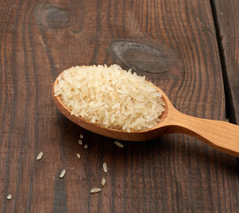 white raw rice in a wooden spoon on a brown table