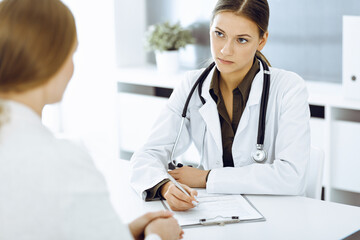 Woman-doctor and patient sitting and talking at hospital office. Green color blouse suits to therapist