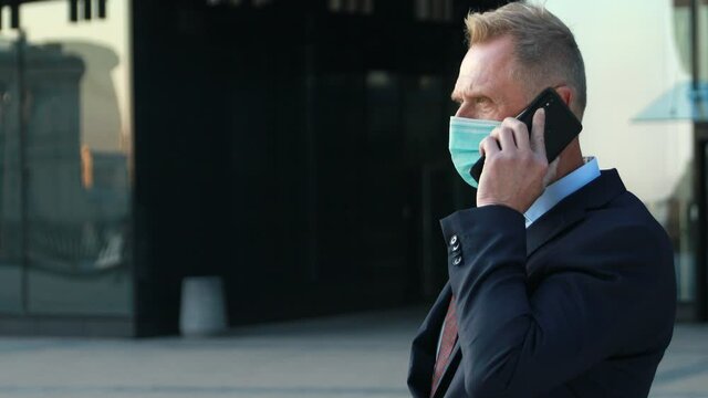 Portrait of confident business man in blue medical mask in classical suit talking on the phone, having business conversation, during a pandemic