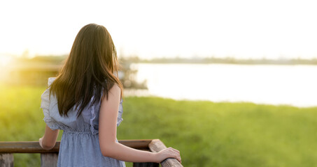 back side of a young girl  standing on a wooden balcony watching sunset or sunrise on the river alone with text space