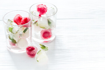 Cocktail glasses with berries in ice cubes on white table copy space
