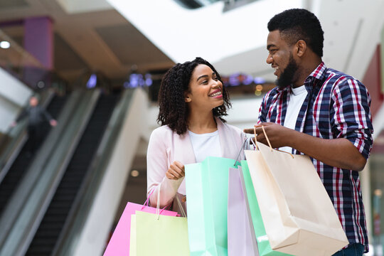 Happy African Couple Spending Time Together In Shopping Mall, Holding Colorful Bags