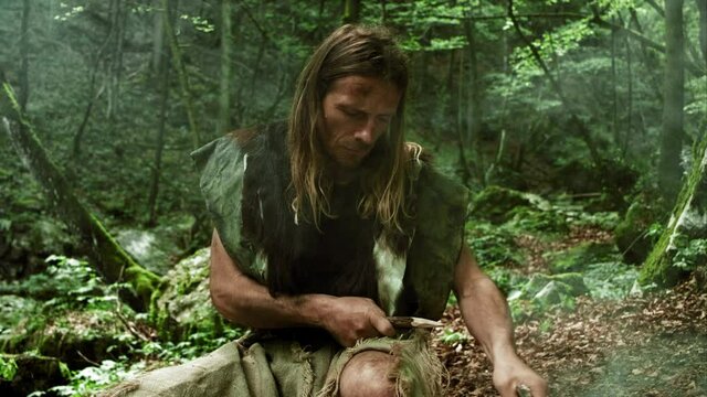 Prehistoric Man Sharpening Wooden Spear Holds It At Arm’s-Length To Admire It