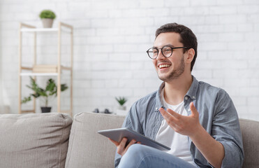 Blogger in workplace. Laughing guy in glasses with tablet in hands explains something