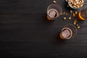 Two glasses of unfinished beer and bottle. Pistachios, chips and nachos in glass plates and scattered