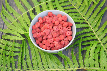 Ripe raspberries in a plate on a background of fern