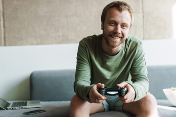 Photo of man playing video game with joystick while sitting on sofa