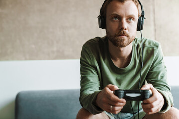 Photo of man playing video game with joystick while sitting on sofa