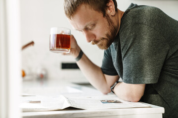 Photo of serious redhead man reading newspaper while drinking tea