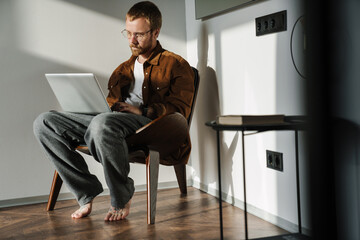 Photo of young man working with laptop while sitting in armchair
