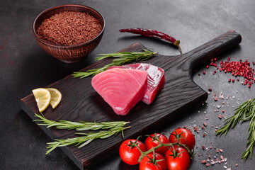 Fresh tuna fillet steaks with spices and herbs on a black background