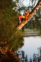 beautiful girl on a tree over water at sunset