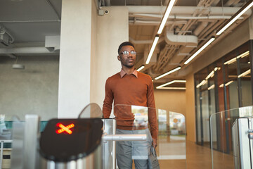 Portrait of young African-American man swiping ID car while passing automated gate to enter office building or college, copy space