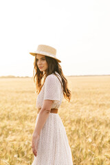 Photo of beautiful brunette woman in straw hat walking on wheat field