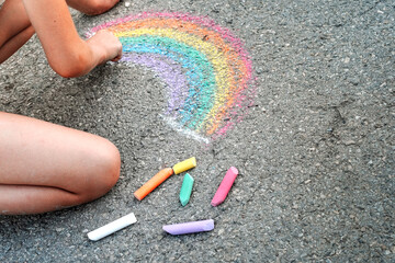 Little girl child draws a rainbow on the asphalt using crayons, world and social concept, place for text copy space