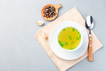 Chicken broth in white cup garnished with chopped parsley, horizontal, top view, copy space