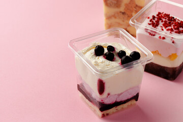 Mousse desserts in square plastic boxes with different toppings on pink table
