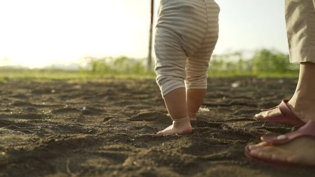 baby first step outdoor walking. mother help her baby to walk her first step on a sand