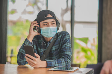 New normal Asian man use face mask listening music by tablet mobile internet