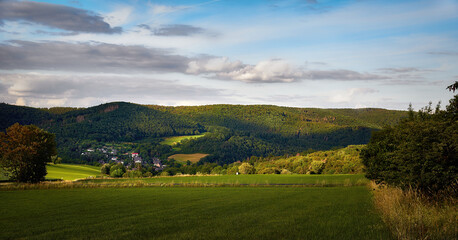Obraz premium Foto eines Dorfes in einem Tal der Berge. Nationalpark Eifel.Das Foto wurde am Abend bei Sonnenuntergang aufgenommen. Dorf, schöne Häuser in einem Tal in den Bergen. Schöne Wiesen und Wald. Berge, N