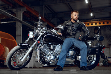 Fototapeta na wymiar Bearded motorcyclist in black leather clothing with his motorbike