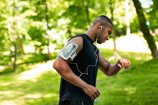 Side View Of African American Jogger Checking Smartwatch Or Fitness Tracker During Morning Run At Park