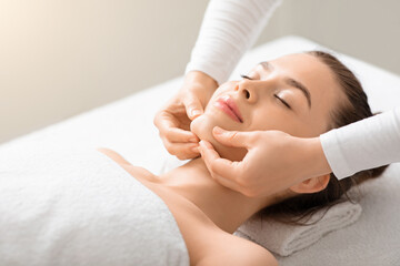 Relaxed young lady having lifting face massage at spa