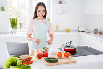 Obraz na płótnie Canvas Photo of asian ethnicity housewife mixing fresh vegetables salad ingredients cooking tasty vegan meal using online blogger recipe notebook on table stand kitchen indoors