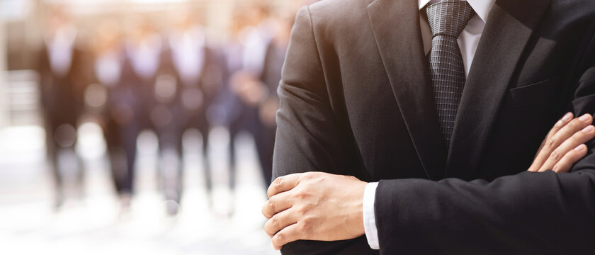 Portrait of a CEO businessman standing hand cross arm successful business team in a classic black suit with employee in background. 