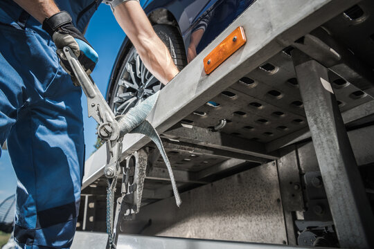 Worker Securing Car On Towing Truck With Tie Down Belts