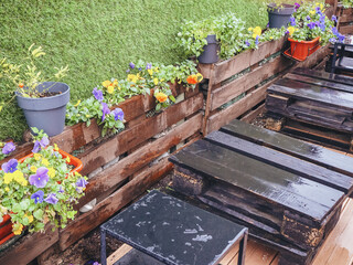 Wooden pallets wet from the rain stand near a wooden border with flowers next to a wall with a decorative green artificial grass coating