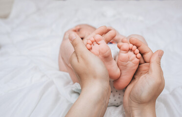 Obraz na płótnie Canvas A caring and loving mother holds in her hands the legs and fingers of a small, newborn, sleeping baby on the bed close-up. Woman's happiness. Photography, concept.