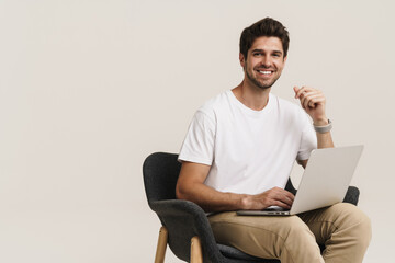Portrait of laughing man working with laptop while sitting on armchair
