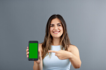 Beautiful brunette Turkish woman pointing an empty smart phone screen for design and advertisement purposes with grey background studio