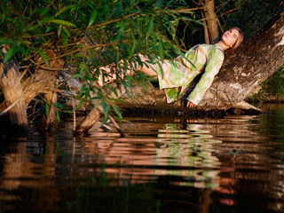beautiful girl on a tree over water at sunset