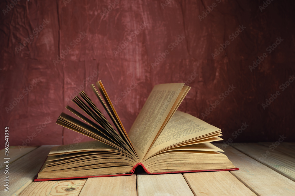 Poster beautiful ancient open old book on a red wooden table and dark-red wall background behind.