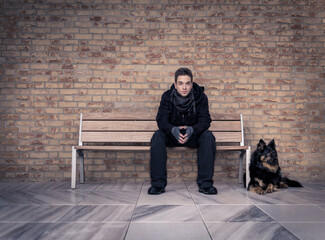 A young man, with his black dog next to him, sitting on a modern bench in a room with a marble...