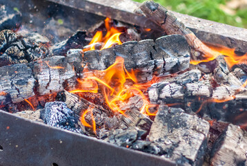 Red-hot pieces of coal and flames in a cooking brazier. Grill with burning coals. Fire and heat.