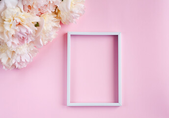 Flat lay with beautiful bouquet of cream peonys and white vertical frame on pink background. Close up. Top view. Copy space.