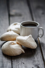 Homemade white meringue cookies and coffee on rustic wooden table.