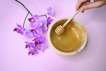 Set of depilation and beauty on pink background concept - sugar paste or hair removal waxing melted paste, orchid and female hands. Sugar paste or honey in a wooden bowl with a special dipper stick.