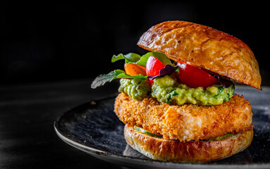 Vegetarian burger with grilled tofu, guacamole sauce and vegetables in plate on black wooden table background