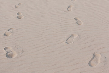 Sandy beach with traces of people’s footstep. Visible texture and fine sand.
