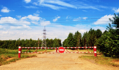 No entry car sign on a striped barrier against a dirt road and blue summer sky 