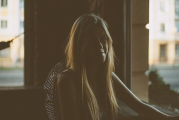 Silhouette of girl with long hair and unusual dress. She is sitting in darkened room, smiling shyly...