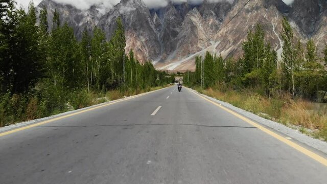Aerial view of a man riding his motorbike on a national road from the Passu Cones, in a stony landscape composed of trees, peaks and mountains during a foggy day, Gilgit Baltistan region