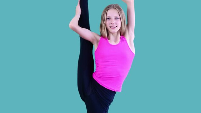 Beautiful young blonde acrobat demonstrating her flexibility, looking straight at camera, standing on one leg, making gesture of caution, block, warning sign. Isolated on blue background. 