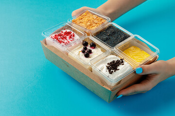 Mousse desserts in square plastic boxes with different toppings on pink table