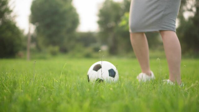 Games And Entertainment, Sport, Physical Culture, Parks And Open Air Concept - Close-up Women's Legs In White Sneakers And Skirt Play Football With Black And White Ball On Green Lawn In Park At Sunset