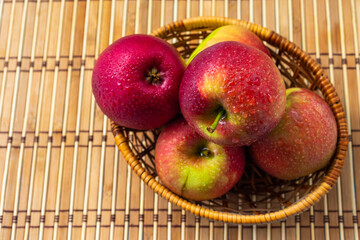 Red apples covered with dew in a wicker basket.